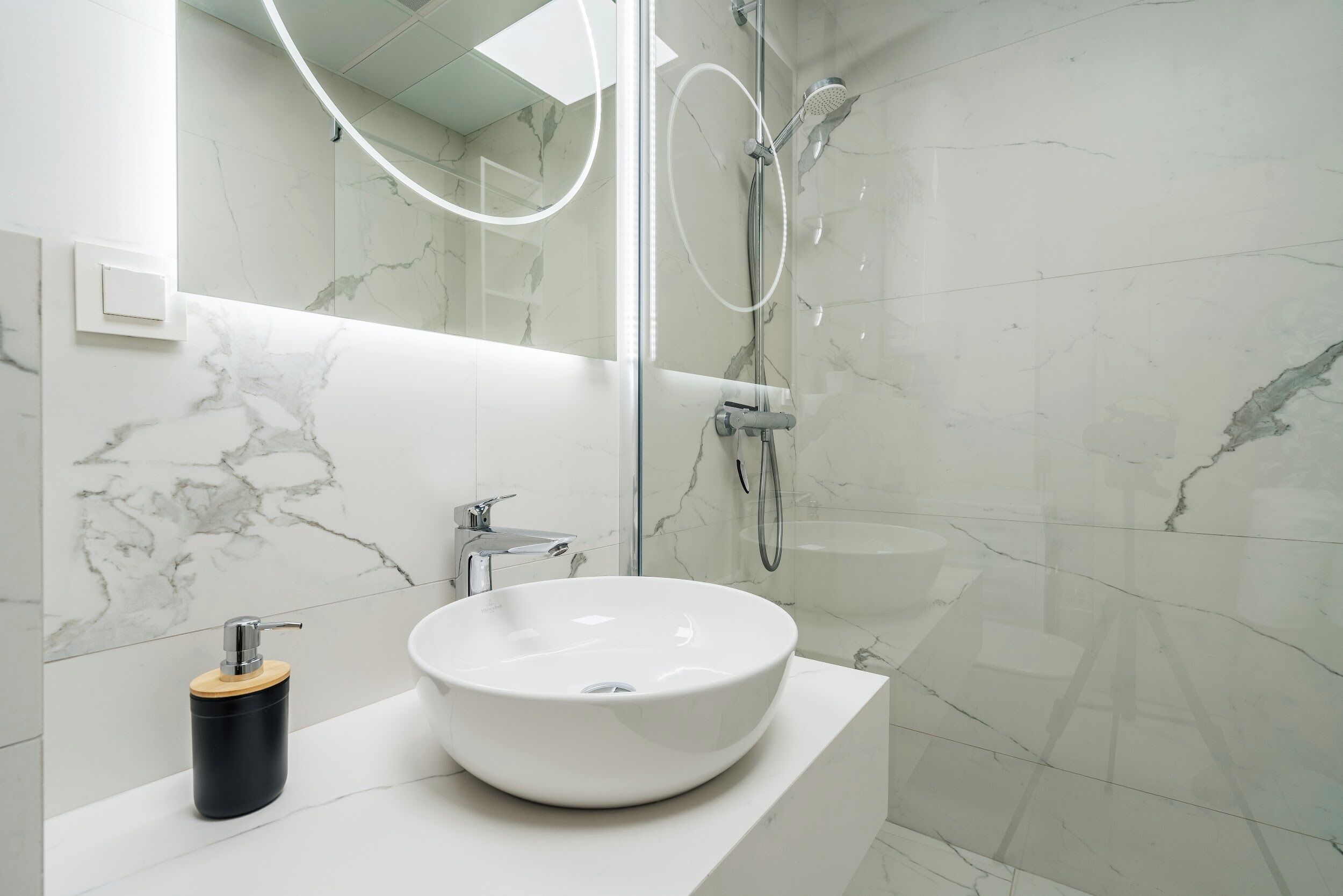 A modern bathroom with a white marble sink, a handheld showerhead, and a glass-enclosed shower.