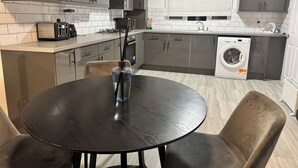 A modern kitchen with grey cabinets, a built-in oven, a washing machine, and a dining area with a round table and two chairs. - Corporate 3bedroom home with parking (Erith)