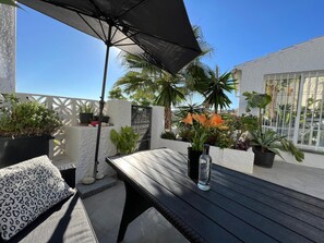 Eine Holzdielen-Terrasse mit Tisch und Stühlen, umgeben von Kübelpflanzen und einem großen Sonnenschirm.