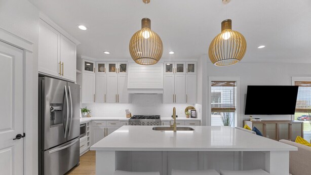 Una cocina moderna con armarios blancos, electrodomésticos de acero inoxidable, una isla central con taburetes altos e iluminación colgante.
