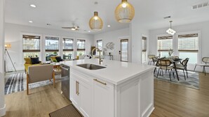 Una cocina moderna con una isla grande, luces colgantes y una zona de comedor con sillas y una mesa.