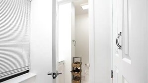 A narrow hallway with white walls, a door with a silver handle, and a window with horizontal blinds. - ★ NEWLY RENOVATED STUDIO IN PRIME LOCATION - UES ★ (New York)