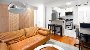 A modern living room with a leather sofa, a dining area with two stools, a kitchen with white cabinets and stainless steel appliances, and a large mirror on the ceiling. - ★ NEWLY RENOVATED STUDIO IN PRIME LOCATION - UES ★ (New York)