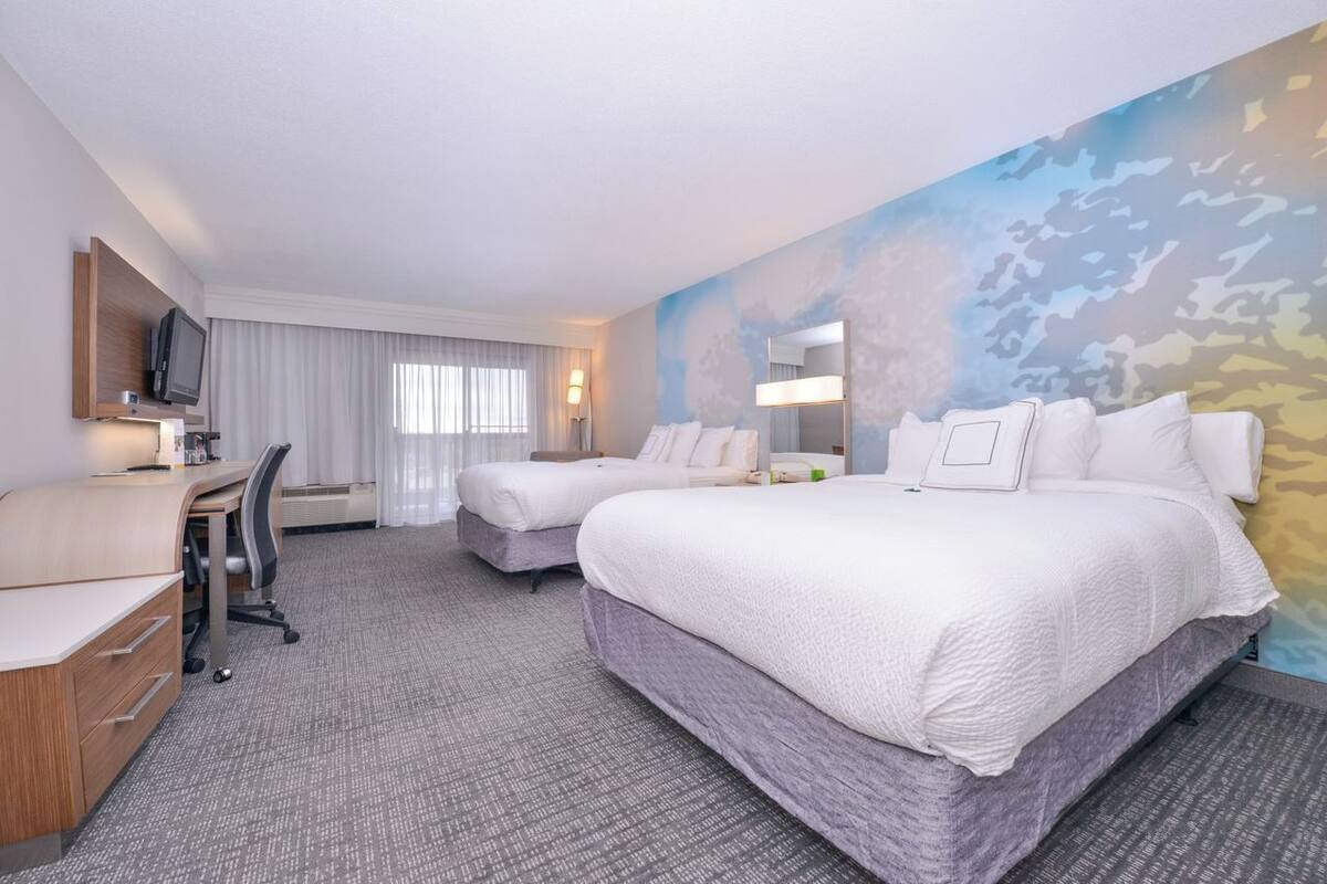 Habitación de hotel con una cama grande, un escritorio, una silla, un televisor y una pared con estampado de camuflaje.