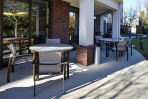 An outdoor patio with round tables and chairs, a brick column, and a glass door leading to a covered area.