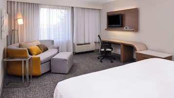Habitación de hotel con cama, sofá, escritorio, silla, televisor y aire acondicionado.