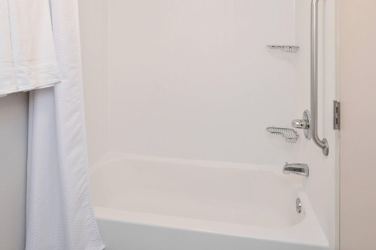 Uma banheira branca com chuveiro e torneira, um porta-toalhas e uma porta.