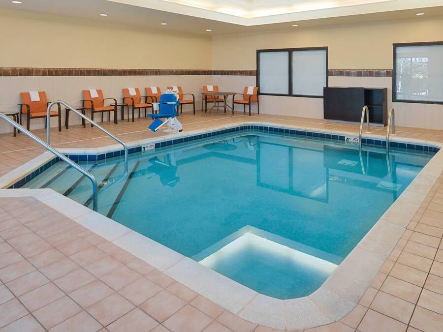 A hotel indoor pool with a tiled floor, a blue pool, and several orange chairs and tables.