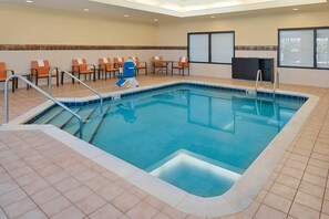 A hotel indoor pool with a tiled floor, a blue pool, and several orange chairs and tables.