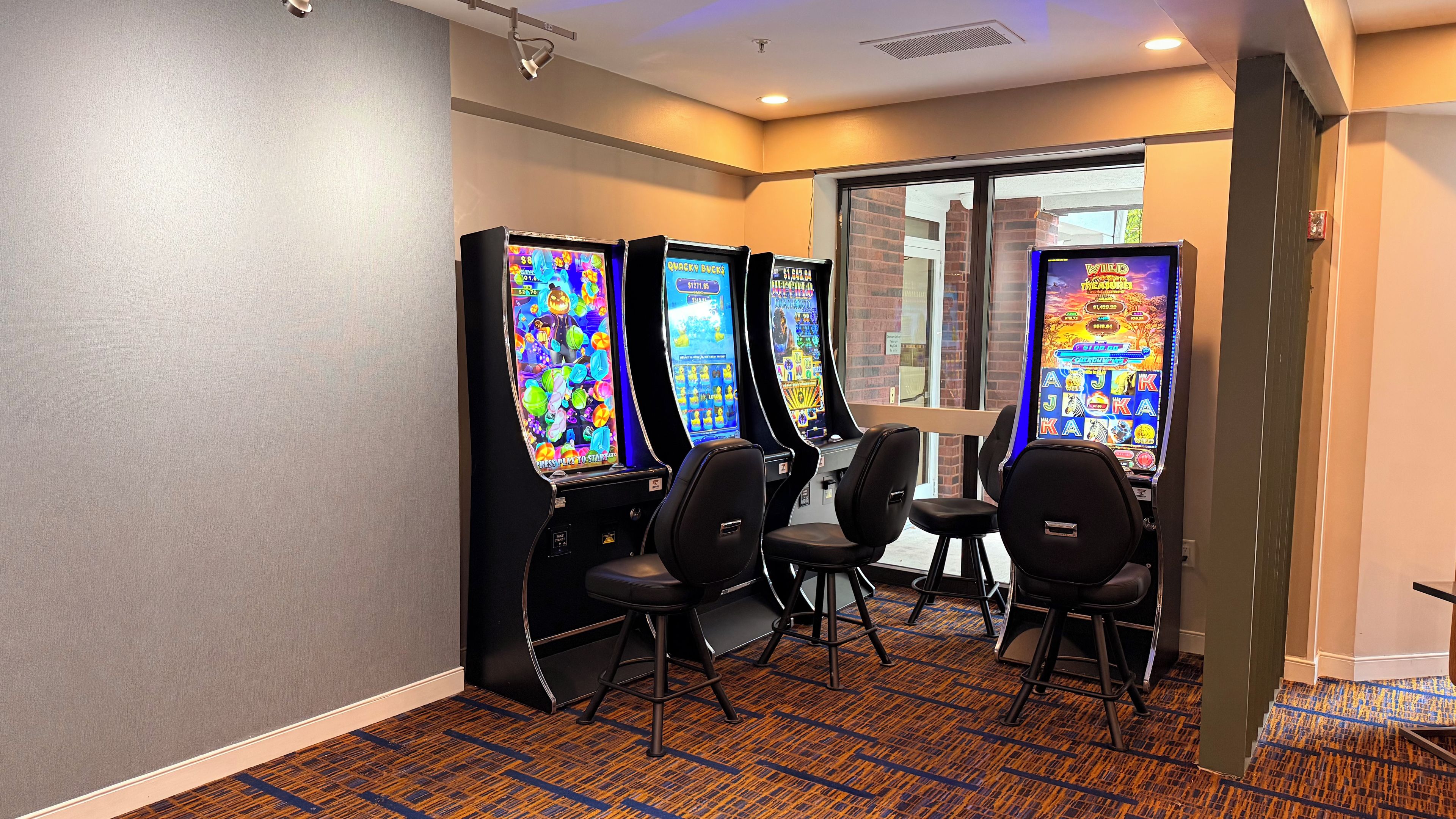 A room with four slot machines, a window, and a carpeted floor.