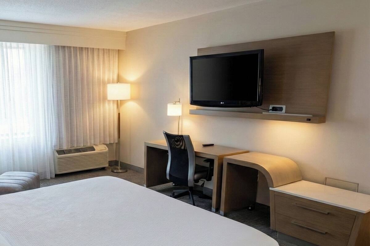 Una habitación de hotel con una cama grande, un escritorio, una silla, un televisor y una lámpara.