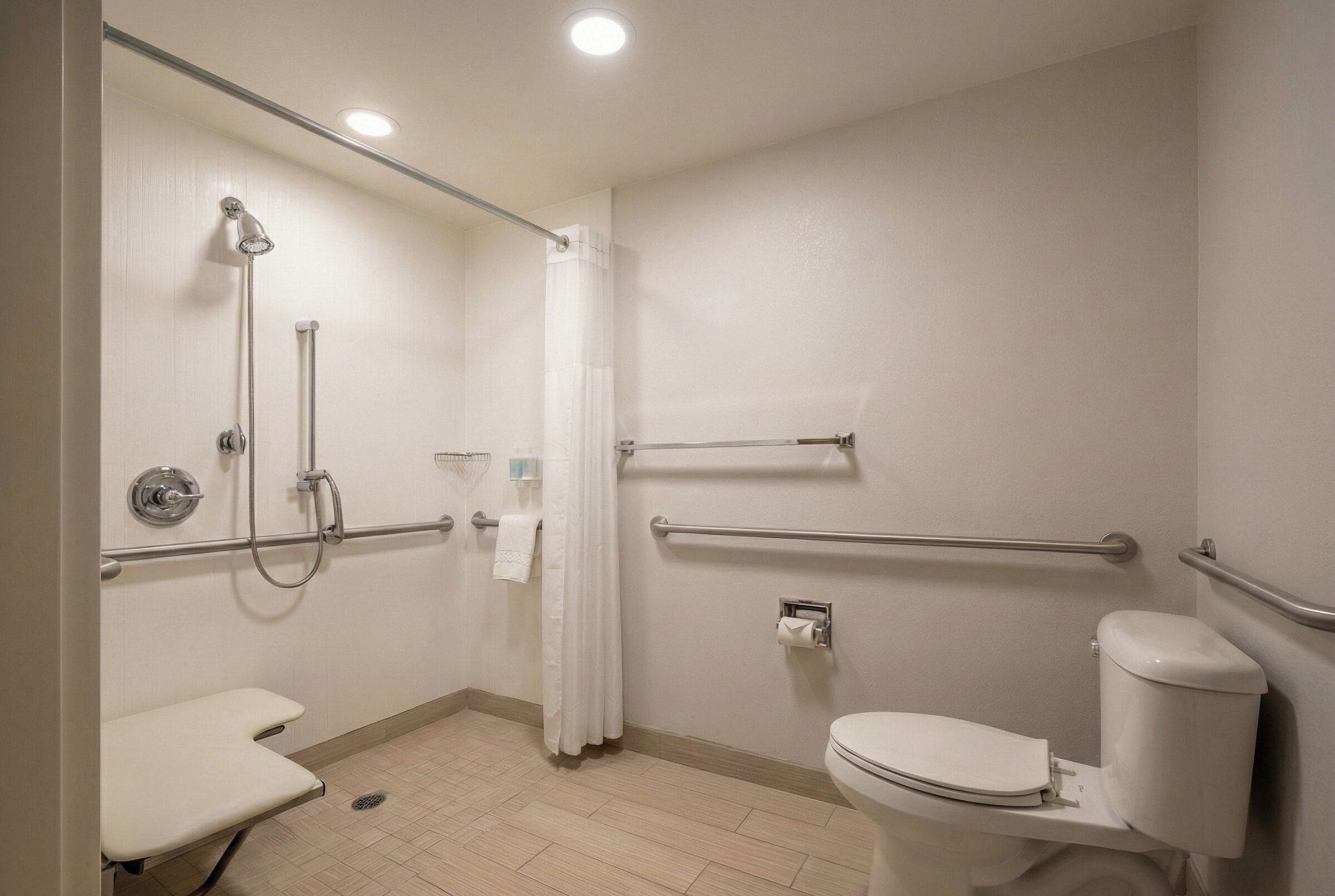 Un baño con ducha, inodoro y barras de apoyo.