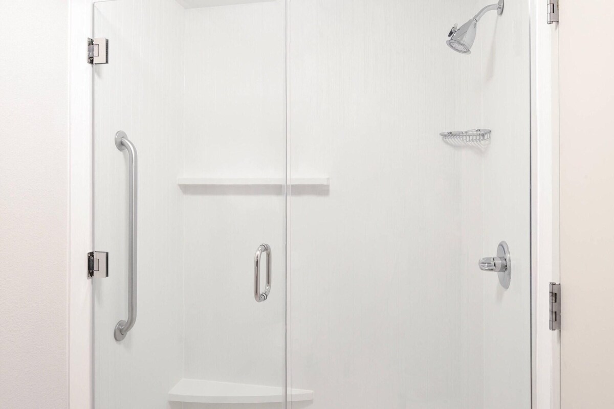 A white shower enclosure with a handheld showerhead, a grab bar, and a shelf.