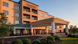 Ett Country Inn & Suites-hotell med en inglasad entré, flera balkonger och en välanlagd trädgård framför hotellet.