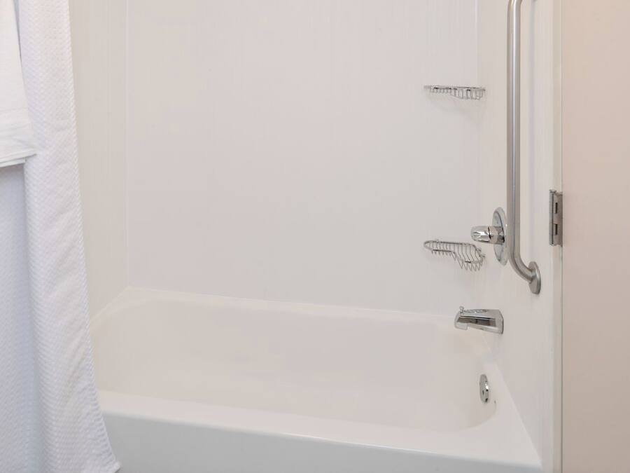 Una vasca da bagno bianca con rubinetteria e soffione cromati, un portasciugamani e un pannello comandi doccia.