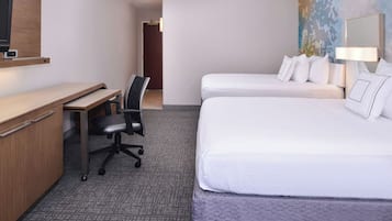 Et hotelværelse med et skrivebord, to senge, en stol, et fjernsyn og et billede på væggen.