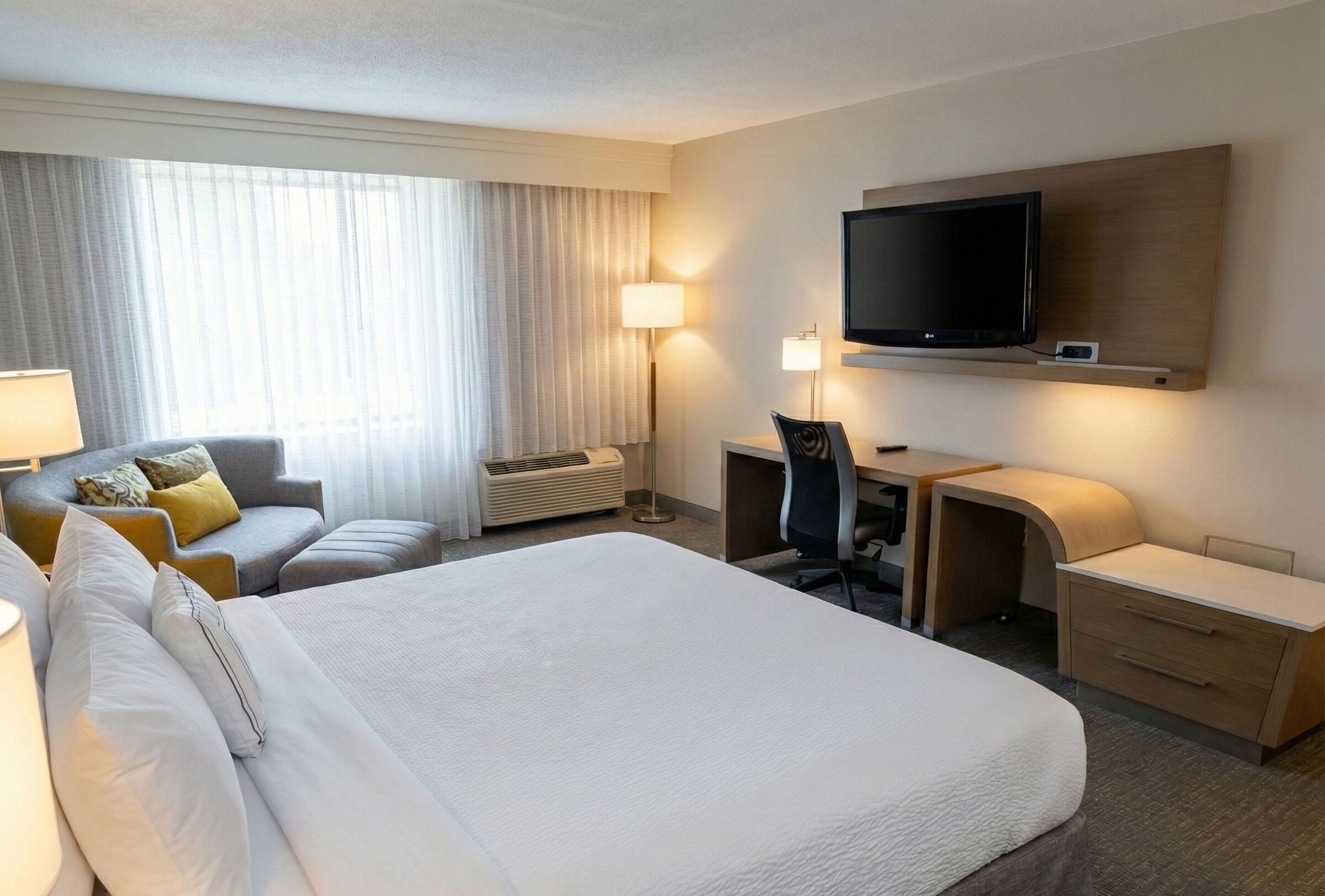 Ein Hotelzimmer mit einem großen Bett, einem Schreibtisch mit Stuhl, einem Fernseher und einem Sofa.