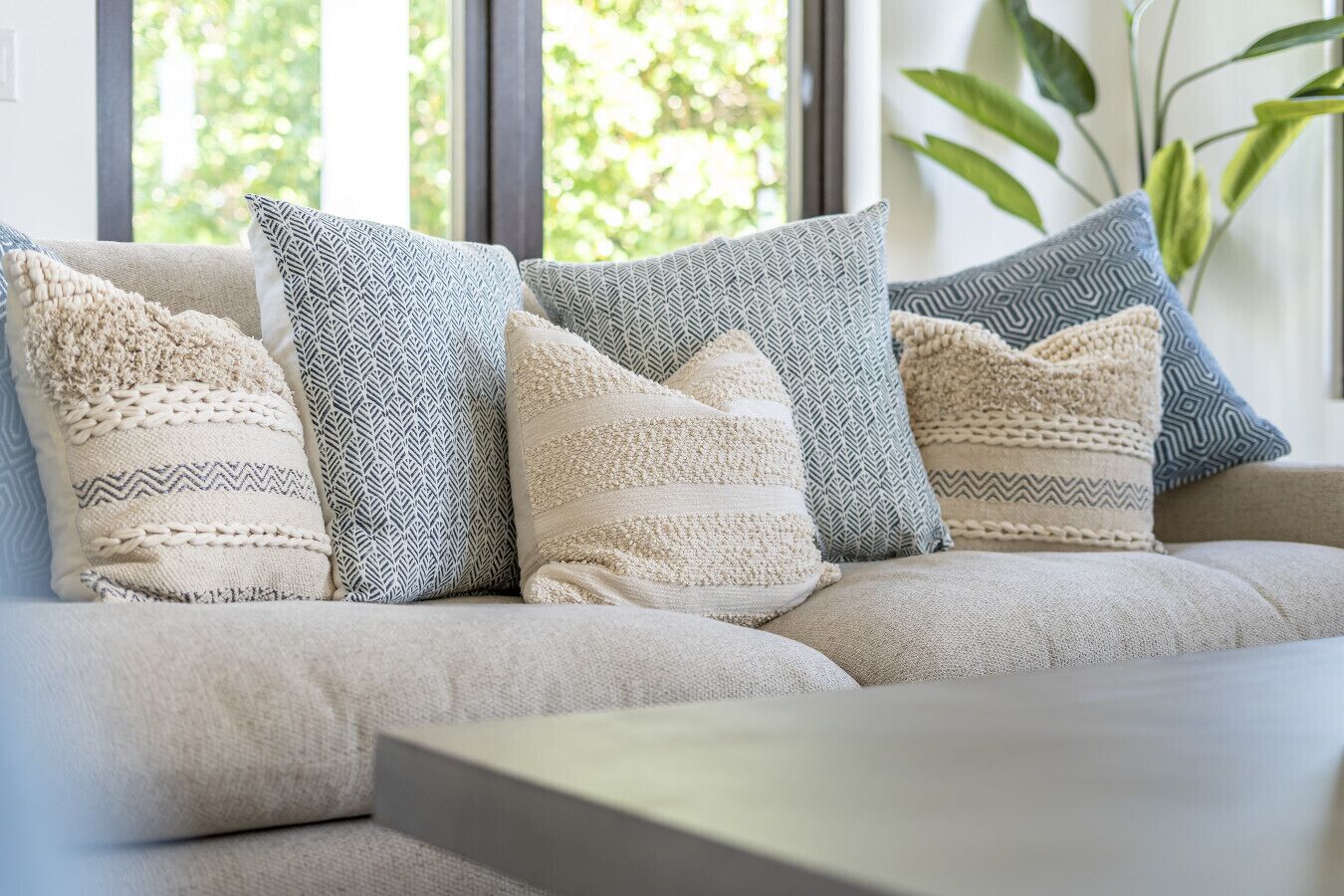 A sofa with multiple patterned cushions in a well-lit room with a large window.