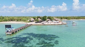 Een resort met een steiger die uitsteekt in helder turquoise water, omringd door weelderige begroeiing en hutten met rieten daken.