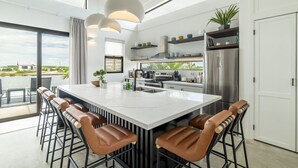 A modern kitchen with a large island, bar stools, stainless steel appliances, and a view of the outdoors. - Villa Seabreeze & Mistico Beach Club + Boat Shuttle (San Pedro)