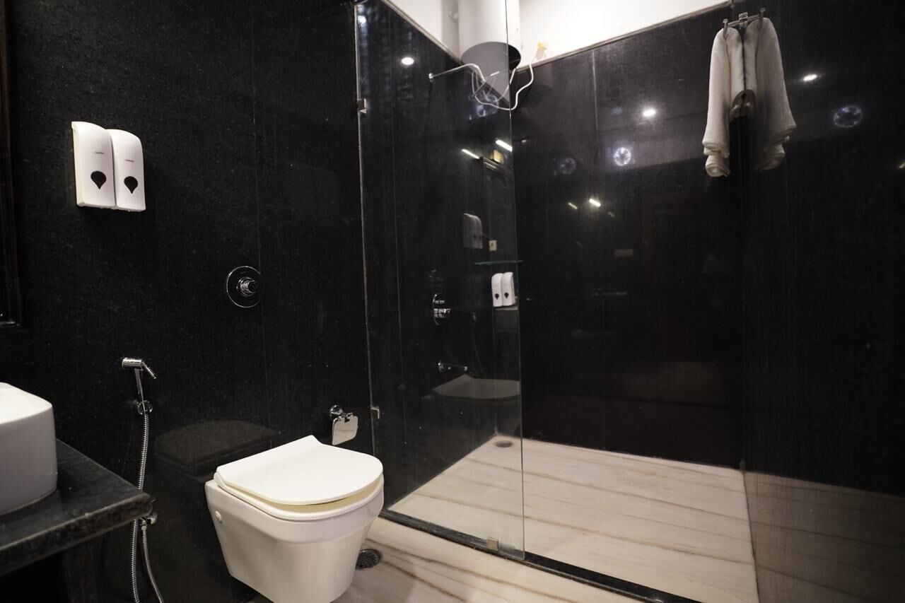 Une salle de bain moderne avec une douche à parois de verre, des toilettes blanches et un mur en marbre noir.