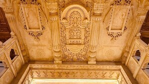 Un plafond architectural richement décoré, orné de sculptures complexes et doté d’un panneau central décoratif.