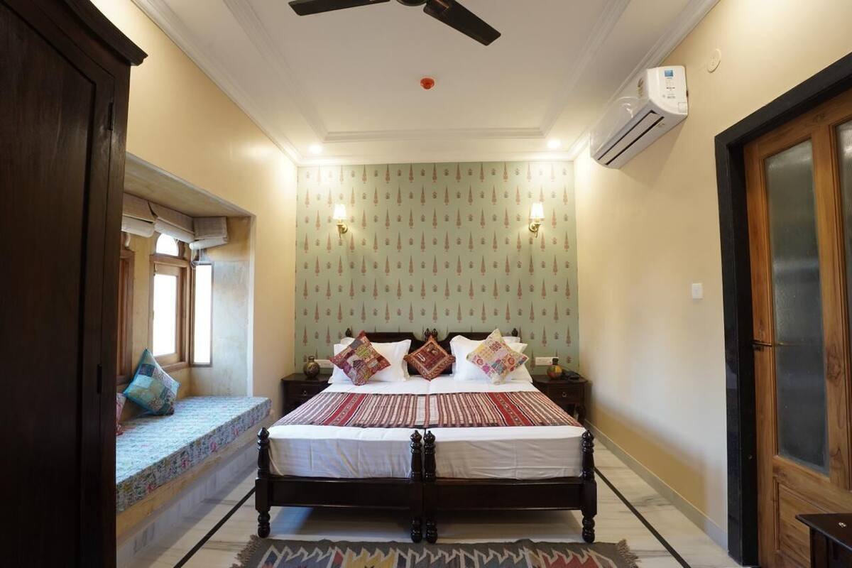 Un dormitorio con cama, ventilador de techo, equipo de aire acondicionado y papel tapiz estampado.