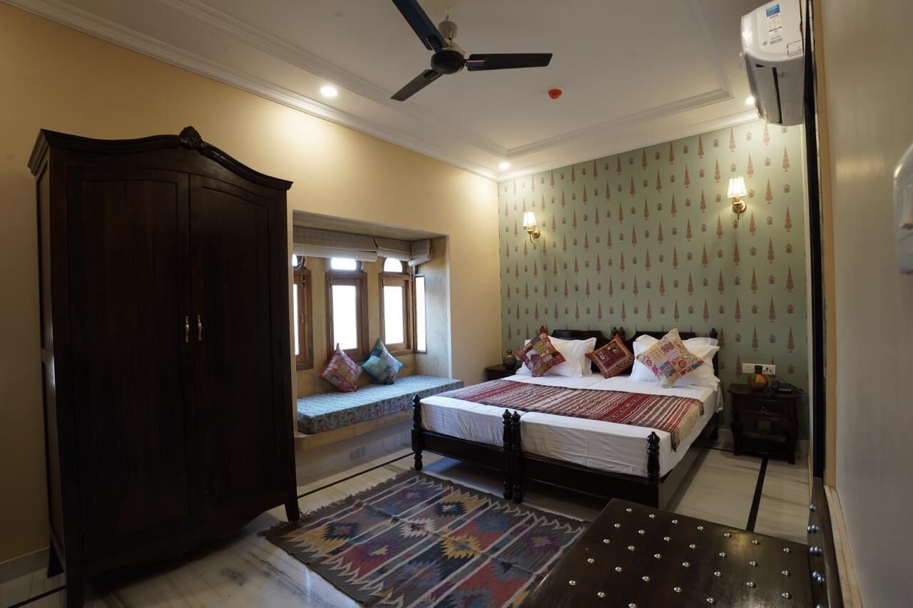 A bedroom with a large wardrobe, a bed with multiple pillows, a ceiling fan, and a wall-mounted air conditioner.