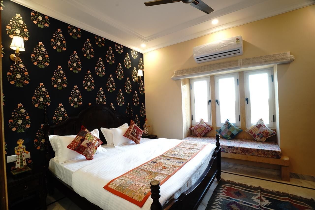 A bedroom with a bed, a bench, an air conditioning unit, and a window with curtains.