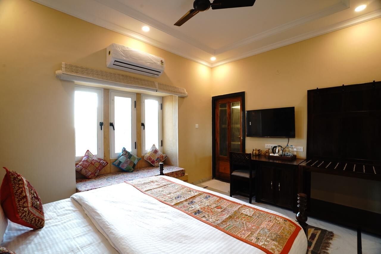 A hotel room with a bed, a desk, a television, and an air conditioning unit.