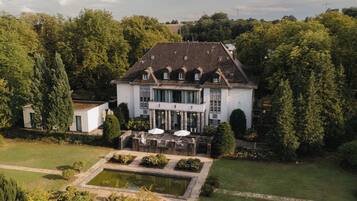 Ein großes, zweistöckiges Gebäude mit einer symmetrischen Fassade, umgeben von üppigem Grün und einem formalen Garten mit einem zentralen Wasserspiel.