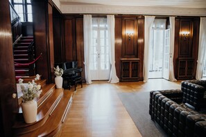 A grand room with a piano, a red carpeted staircase, and a black leather sofa. - Villa Weißer Berg (Neuwied)