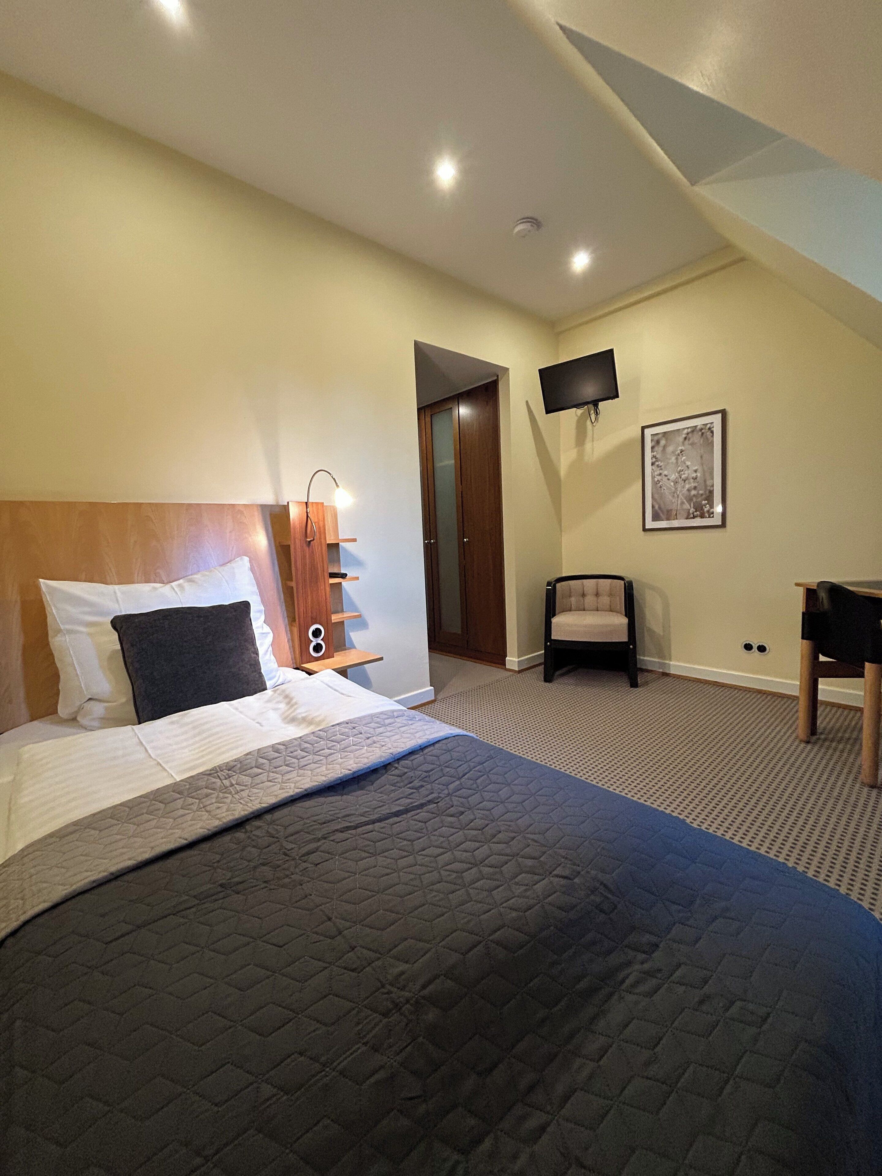 Ein Hotelzimmer mit einem Bett, einem Sessel, einem Schreibtisch, einem Fernseher und einer Tür.