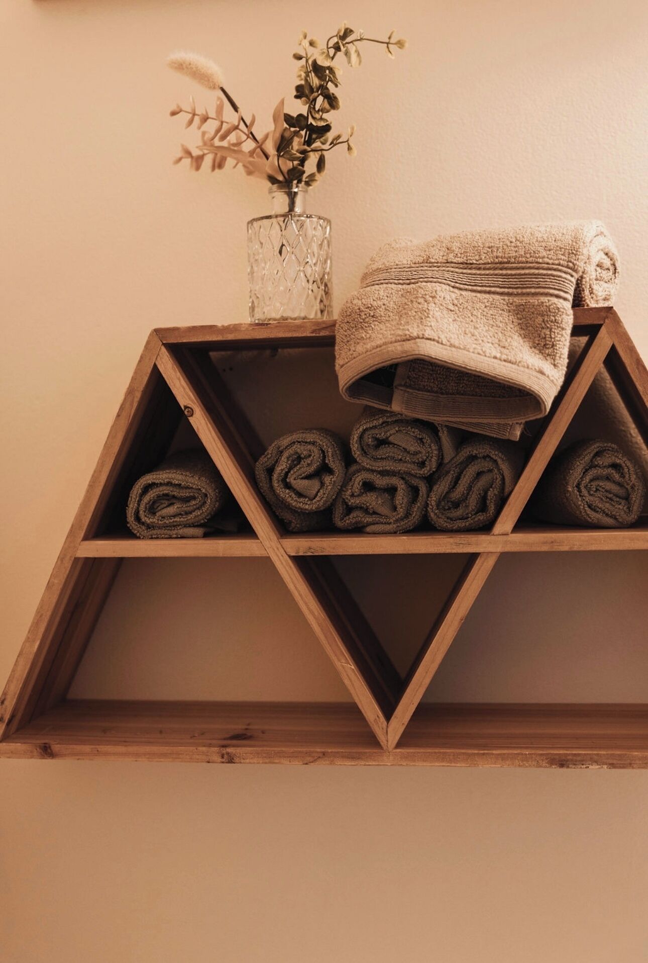 A wooden shelf with rolled towels and a vase with dried flowers.