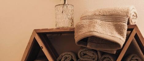 A wooden shelf with rolled towels and a vase with dried flowers.