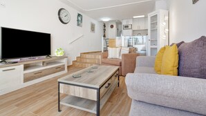 Ein modernes Wohnzimmer mit Flachbildfernseher, Couchtisch, Sofa und einer Treppe, die zur Küche führt.