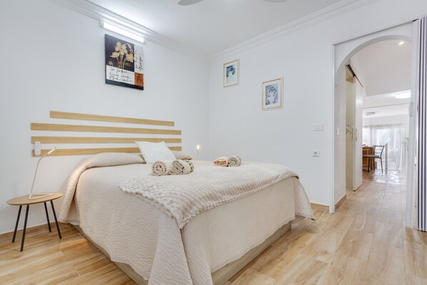 A bedroom with a bed, a bedside table, a wall-mounted lamp, and artwork.