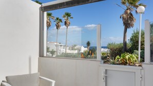Ein Balkon mit weißem Stuhl, Blick auf Palmen und ein Gebäude im Hintergrund.