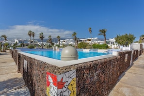 A swimming pool with a stone wall, palm trees, and modern buildings in the background.