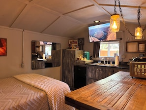A compact kitchen with a wooden table, a sink, and a television mounted above it.