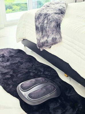 A bed with a white mattress and a gray blanket, a black rug, and a black footrest.