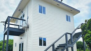 Un edificio de dos pisos con balcón, escaleras y un equipo de aire acondicionado.