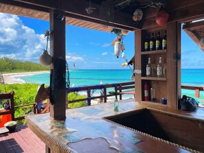 A wooden bar with a view of the ocean, a shelf with bottles, and a hanging net.