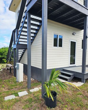 Ein modernes Haus mit überdachter Veranda, einer Treppe und einem kleinen Garten.
