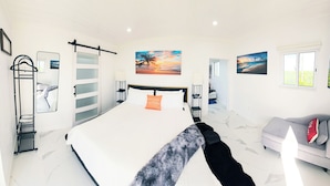 Un dormitorio con una cama, un sofá gris, un espejo, un cuadro y una ventana.