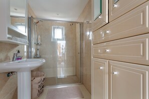A bathroom with a glass shower enclosure, a white sink, beige cabinets, and a small window. - Apartment with Sea View and Pool, Wi-Fi Included (La Sabinita)