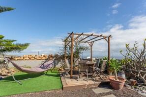 A hammock, wooden pergola, patio furniture, and potted plants in a backyard setting. - Apartment with Sea View and Pool, Wi-Fi Included (La Sabinita)