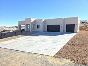 A modern building with a flat roof, large garage doors, and a spacious concrete driveway.