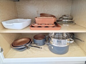 A kitchen cabinet with various cookware items including pots, pans, and baking trays.
