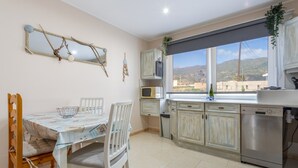 Una cocina con una mesa de comedor, sillas, armarios, lavavajillas, microondas y una ventana con vistas.